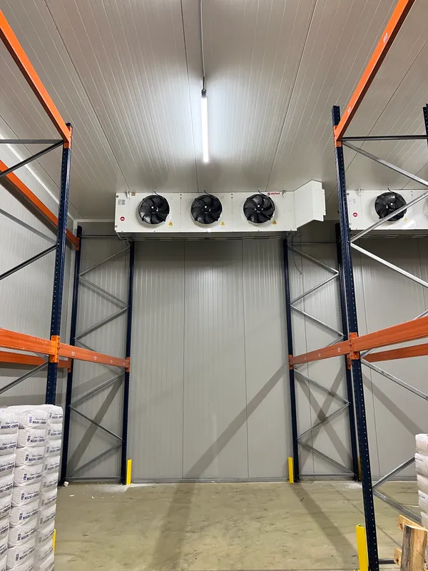 Intérieur d'une chambre froide professionnelle : évaporateur plafonnier à trois ventilateurs, porte coulissante isotherme et rayonnages